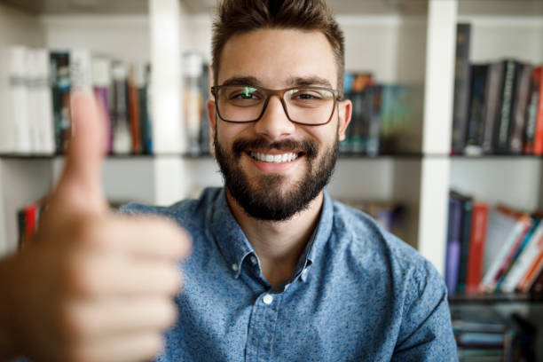 Camera point of view of young man holding thumbs up at home office
